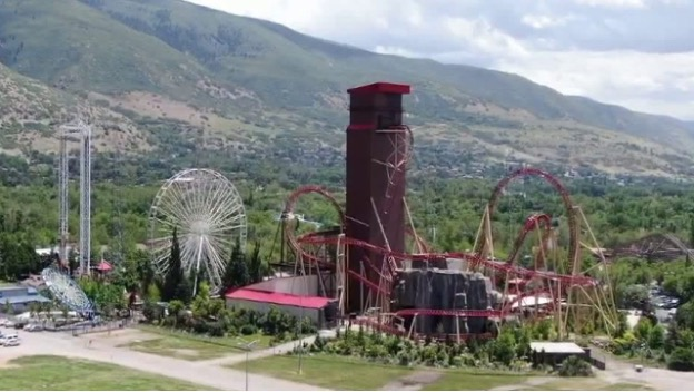 A rollercoaster, Ferris wheel, and drop tower against a background of mountains