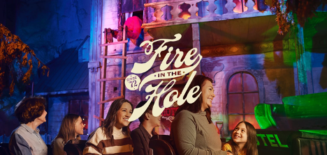 People sit in a roller coaster car and ride past a burning building