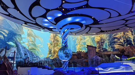 A large LED screen shows images of kelp underwater with an earth globe at the center of the room