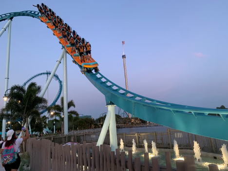 A stand-up roller coaster swoops down into fountains of water