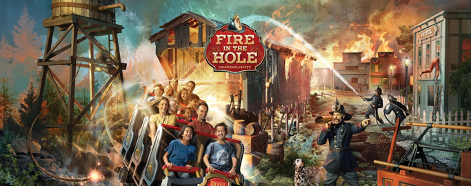 Firemen spray a burning bridge with water as a roller coaster train with happy riders passes through.